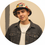 Portrait of Gallucks, a person with dark hair, wearing a GRAFFIX top, against a warm cream background.